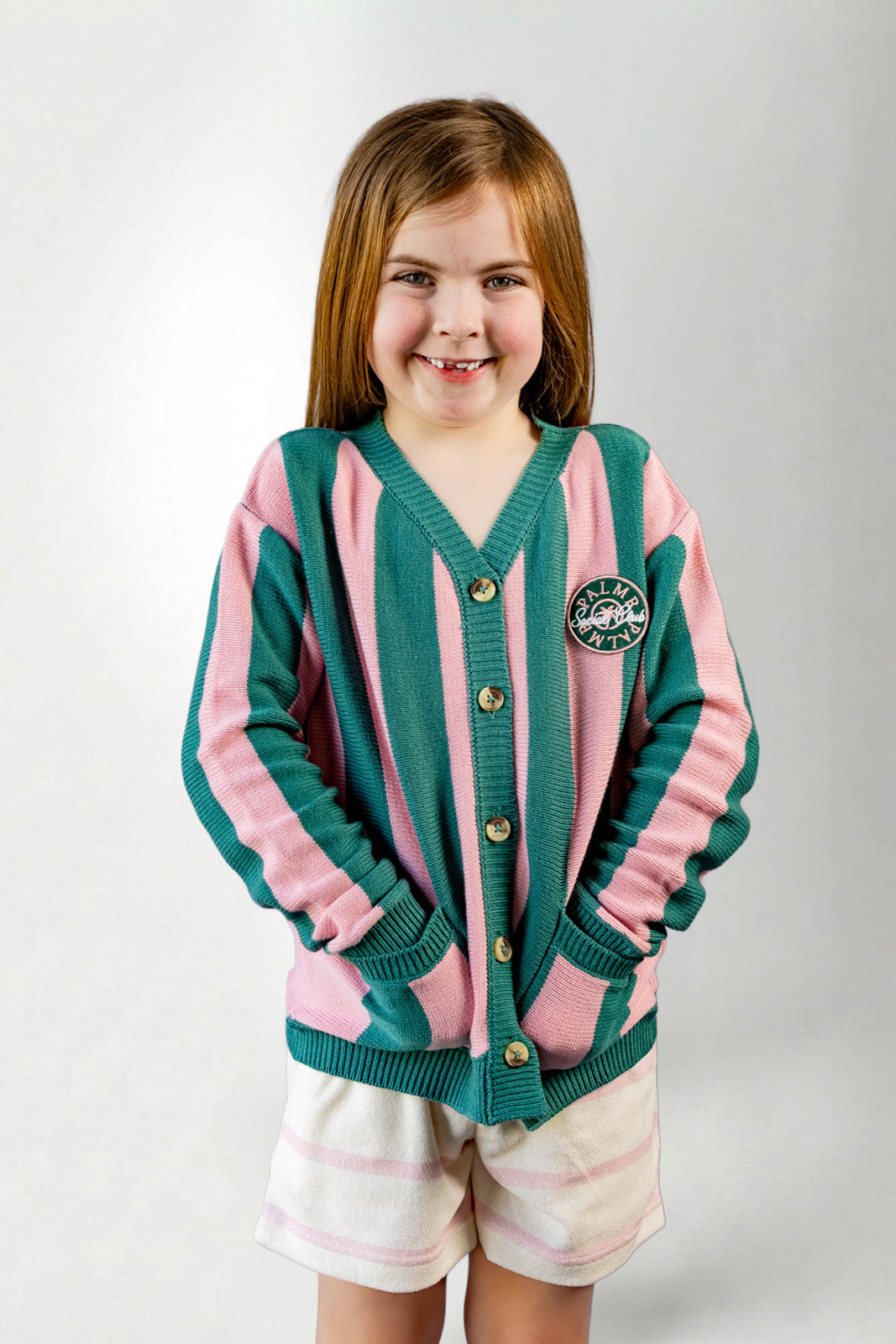 Young girl wearing a green and pink cardigan with a logo on a white background