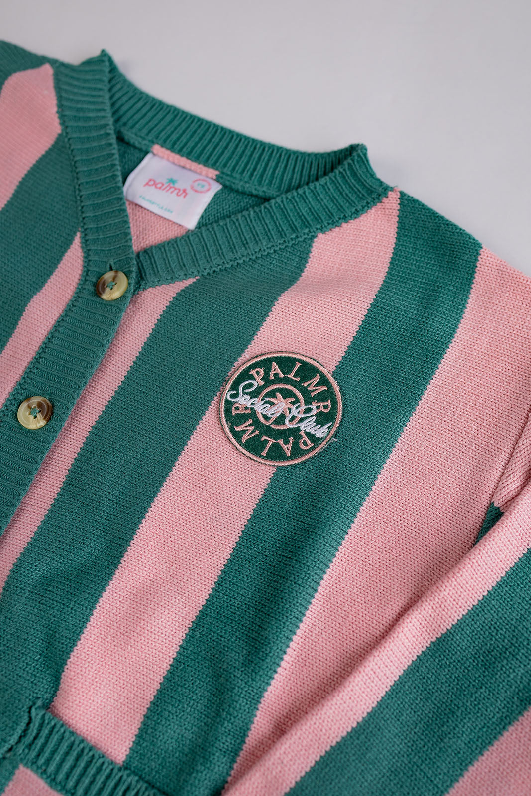 Pink and green striped sweater with a brand logo on a light gray background