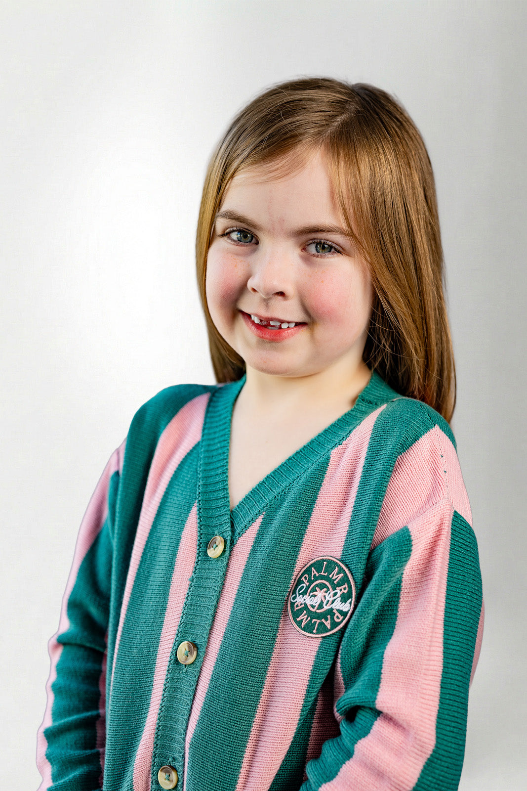 Young girl wearing a pink and green cardigan with a logo on a white background