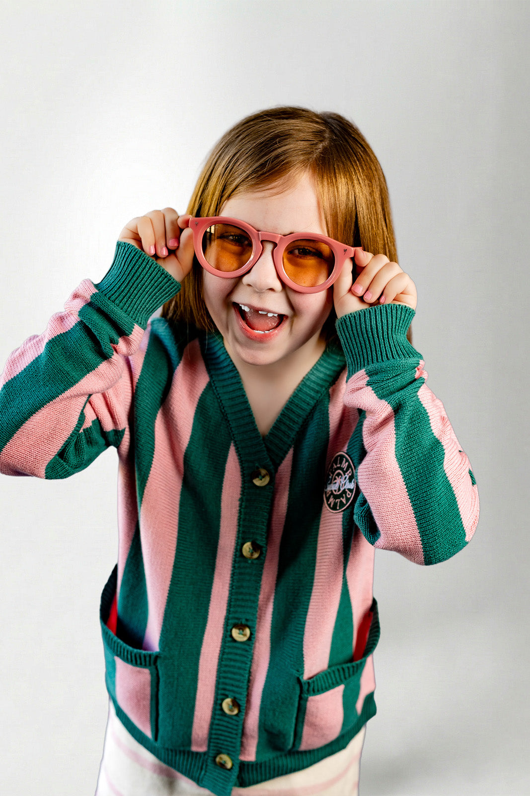 Child wearing a pink and green striped cardigan with sunglasses on a white background