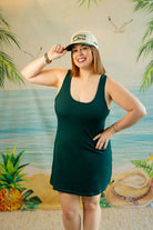 Woman in a green dress and cap posing in front of a tropical-themed backdrop