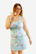 Woman wearing a tropical print dress holding a drink against a white background
