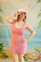 Woman in a pink dress and cap posing in front of a tropical-themed backdrop