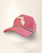 A pink baseball cap featuring a white Florida state silhouette graphic on the front, a green and white patterned decorative band across the brim, and white script embroidery on the side, shown against a plain light beige background.