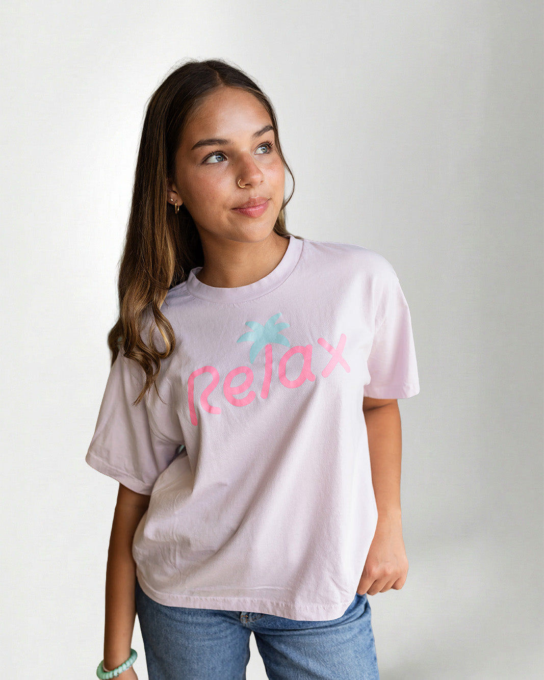 Person wearing a light pink t-shirt with 'Relax' printed on it against a plain background