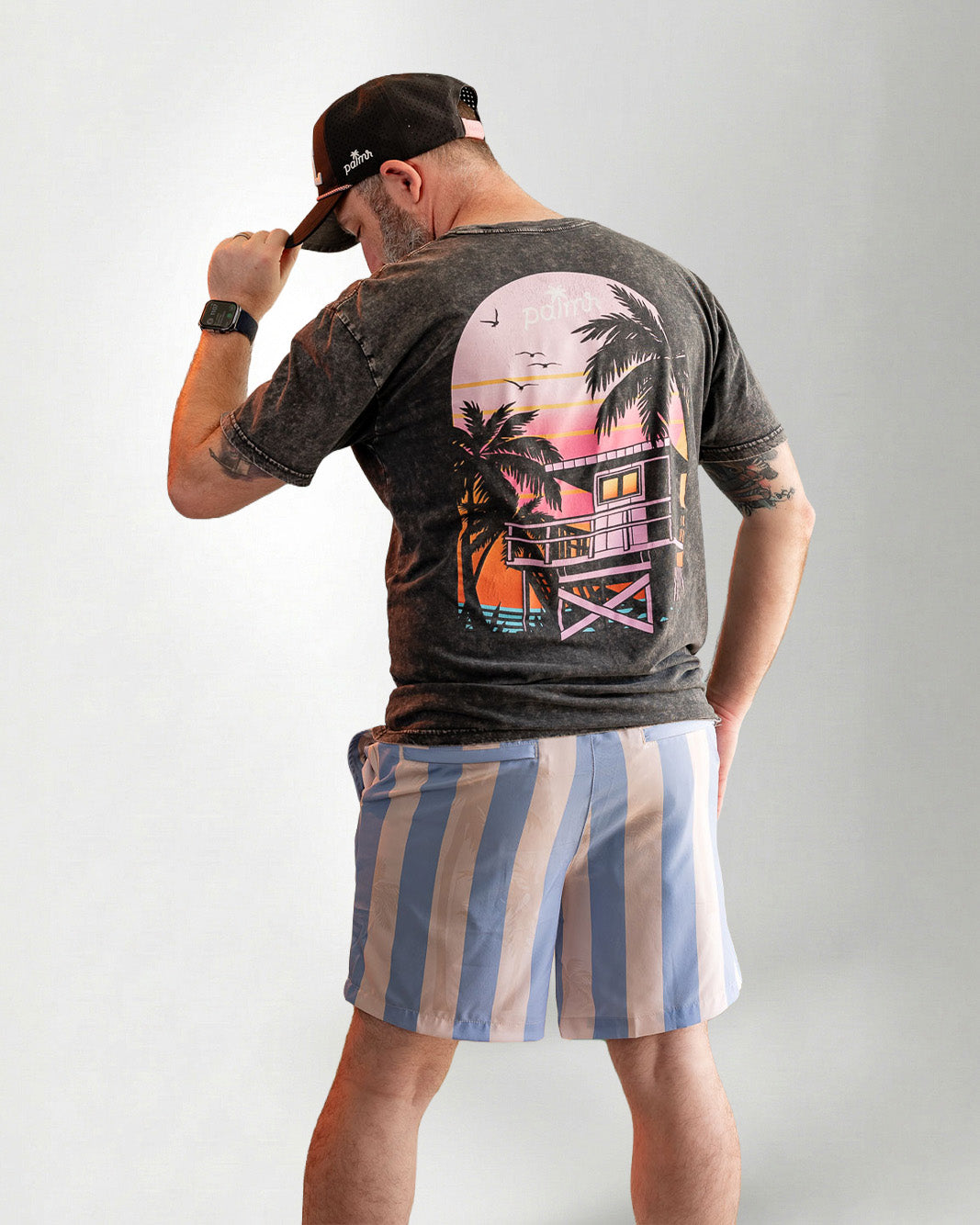 Man wearing Palmr Style Mens Ronnie Hybrid Swim Shorts Blue Tan Stripe Palm leaf Resort Wear and a black tee against a white background 