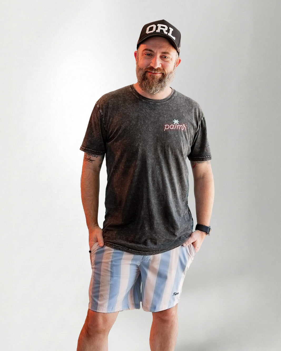 Man wearing Palmr Style Mens Ronnie Hybrid Swim Shorts Blue Tan Stripe Palm leaf Resort Wear and a black tee against a white background 