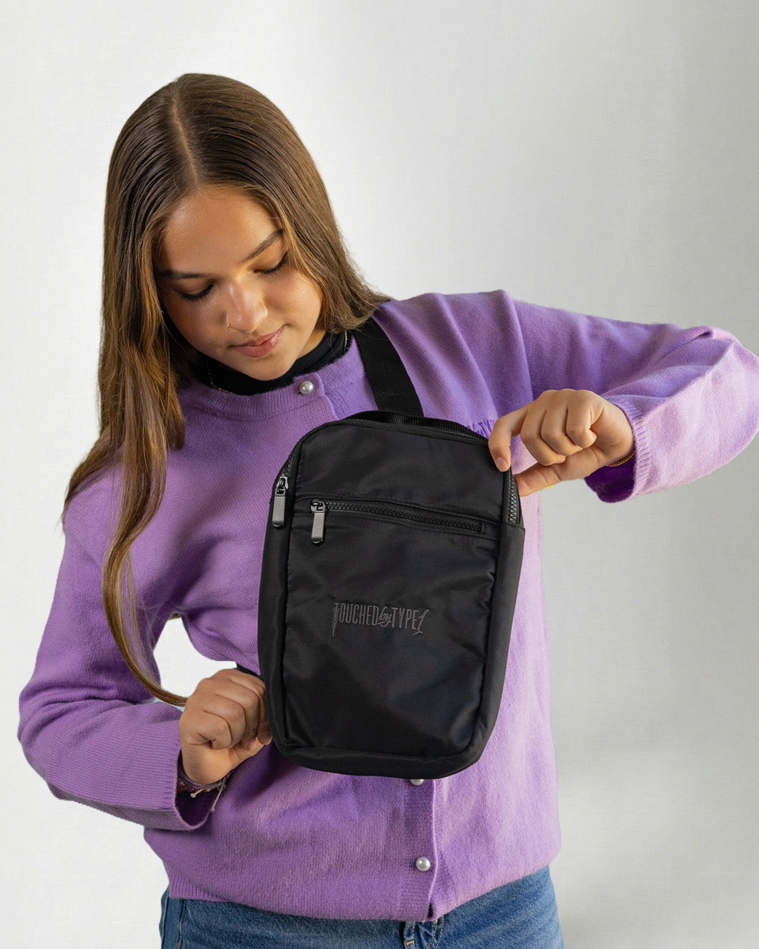Girl using a "Touched by Type one purple cardigan" and a "Touched by type 1" Black crossbody bag against a gray background