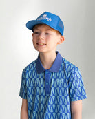 Child wearing a blue patterned polo shirt and cap with a white background