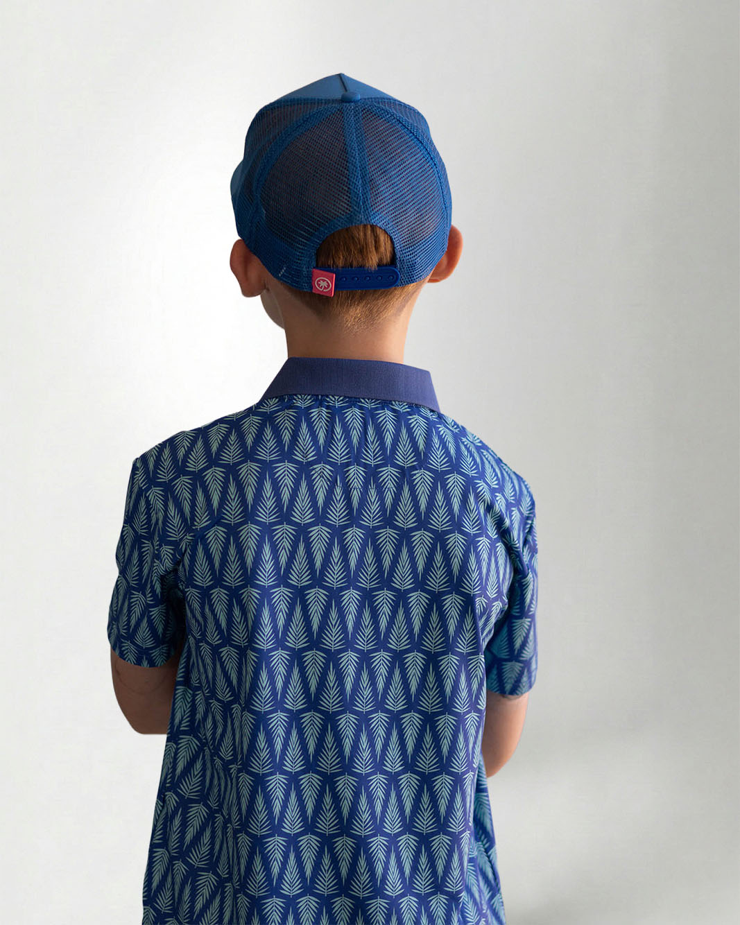 Child wearing a blue patterned polo shirt and cap with a white background