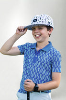 Child wearing a blue patterned polo shirt and cap with a white background