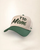 A baseball cap with a light beige crown and a dark green brim, featuring 'TID Mom' embroidered on the front in dark green script, with a small 'Palm.