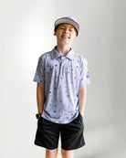 Child wearing a patterned polo shirt and cap on a plain background