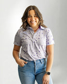 Woman wearing a patterned shirt and jeans against a plain background