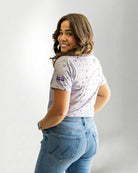 Woman wearing a patterned shirt and jeans against a plain background