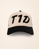 A structured baseball cap with a light beige crown and a black curved brim, featuring the stylized text 'T1D' embroidered in black across the front panels.
