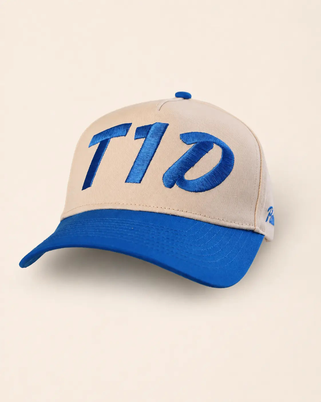 A baseball cap with a beige crown and a bright blue visor, featuring large blue embroidered 'T1D' lettering on the front and a small blue embroidered logo on the side, set against a plain beige background.