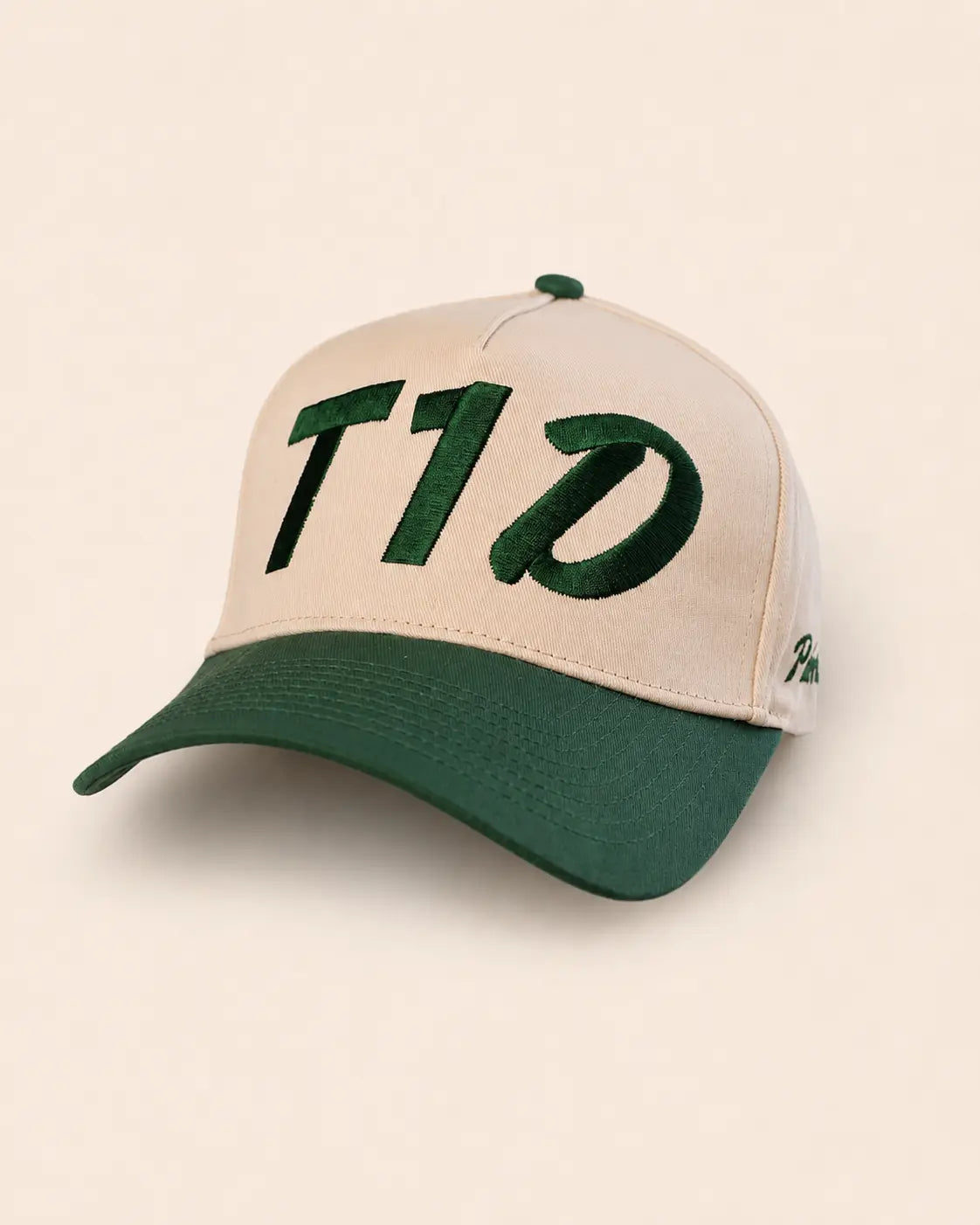 A baseball cap with a cream-colored front panel and brim, and a dark green curved brim and top button. The front panel features large green embroidered letters spelling 'T1D'.