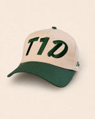 A baseball cap with a cream-colored front panel and brim, and a dark green curved brim and top button. The front panel features large green embroidered letters spelling 'T1D'.