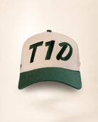 A baseball cap with a light beige crown and a dark green brim, featuring the letters 'T1D' embroidered in dark green across the front panels.