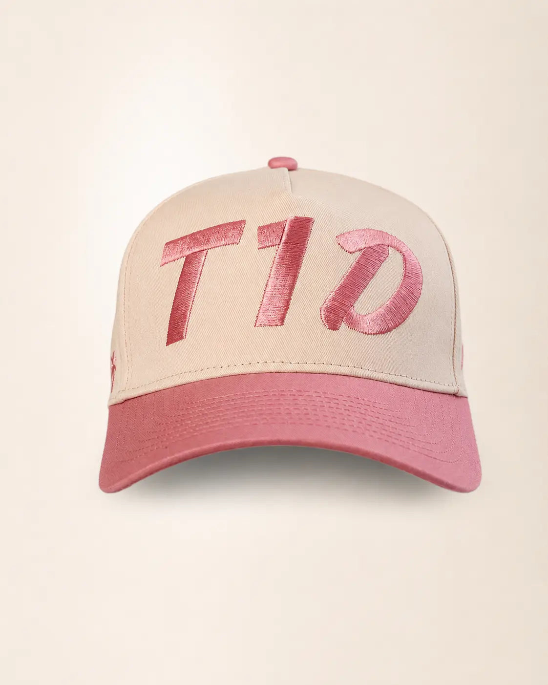A baseball cap with a light beige crown and a dusty pink brim, featuring large pink sequined 'T1D' lettering on the front.