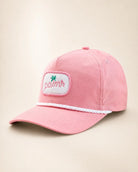 A pink baseball cap with a white embroidered patch on the front featuring the Palmr logo, a white braided rope detail across the brim, and a curved brim, shown against a light beige background.