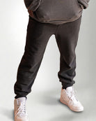 Person wearing a dark gray hoodie and pants with white sneakers on a light gray background