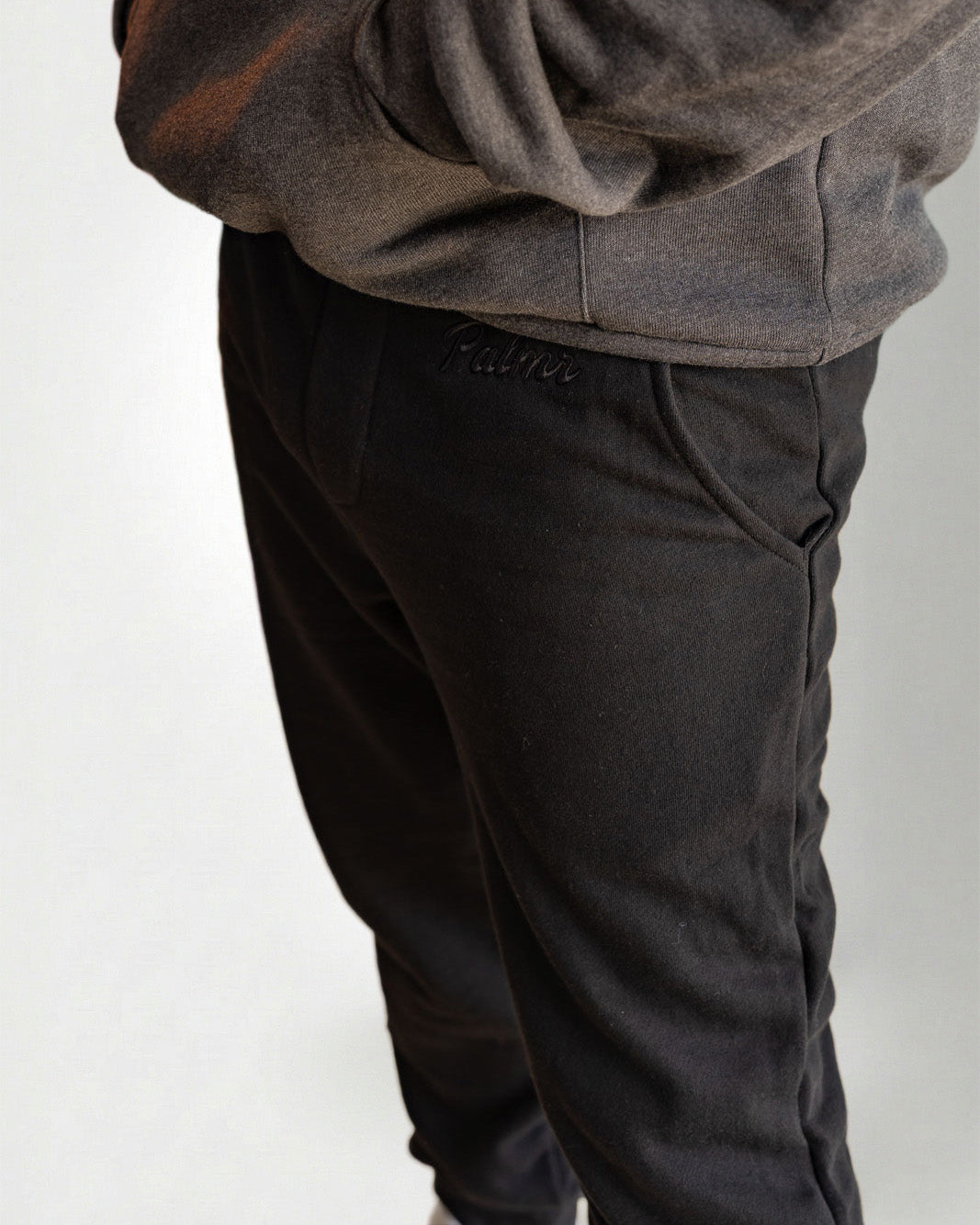 Person wearing a dark gray hoodie and pants with white sneakers on a light gray background