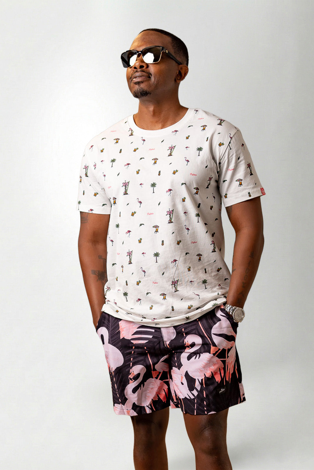 Man wearing a white t-shirt with a pattern and colorful shorts on a plain background