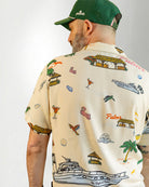 Man wearing a patterned shirt and striped shorts with a cap on a plain background