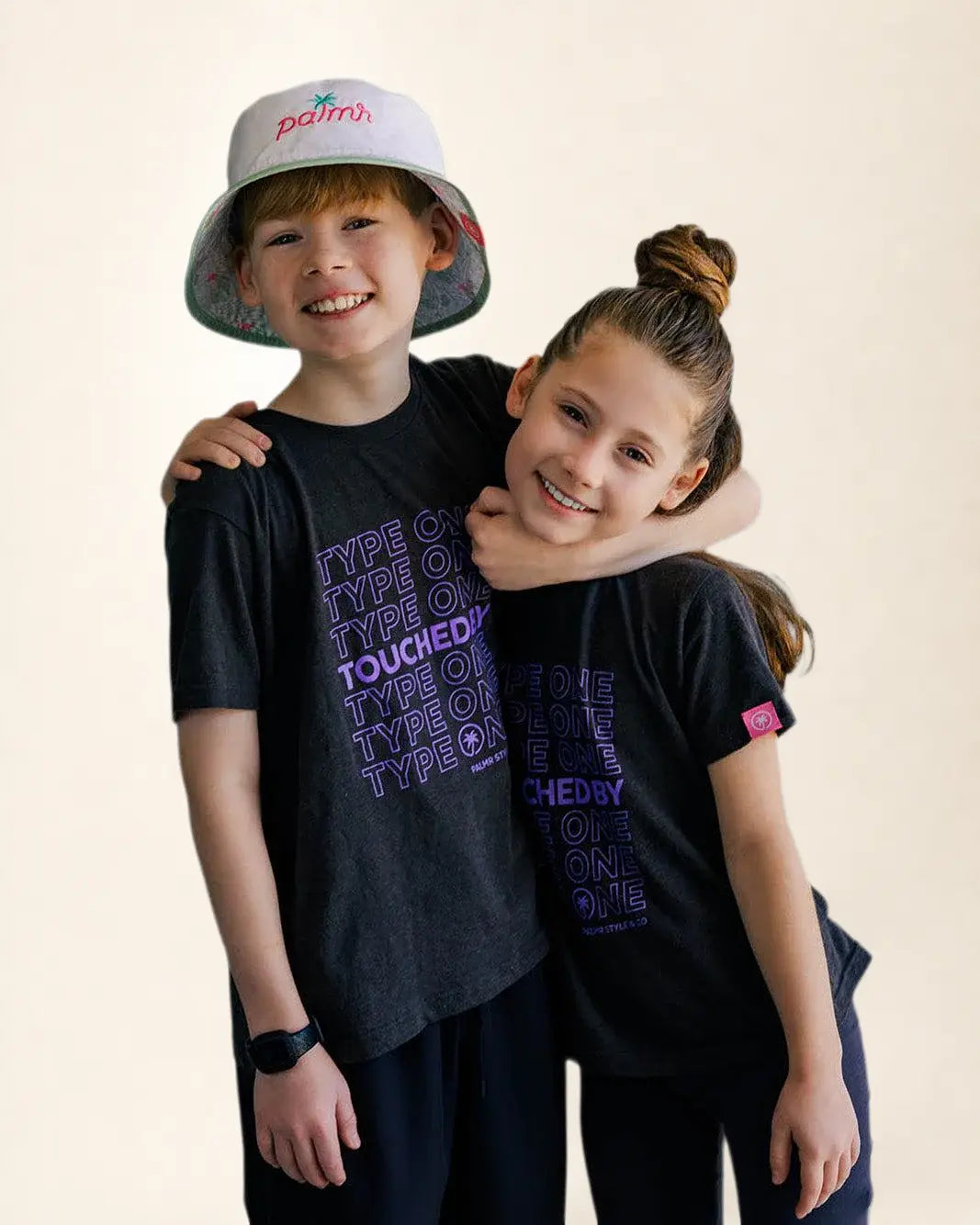 Two children wearing matching black t-shirts with purple text on a beige background