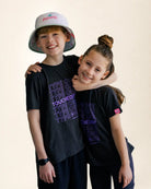 Two children wearing matching black t-shirts with purple text on a beige background