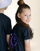 Girl wearing a black t-shirt with a logo on the back, standing next to another person.