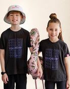 Two children wearing matching black t-shirts with 'TYPE ONE' text, holding a pink flamingo toy.