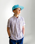 Child wearing a patterned shirt and blue cap against a plain background