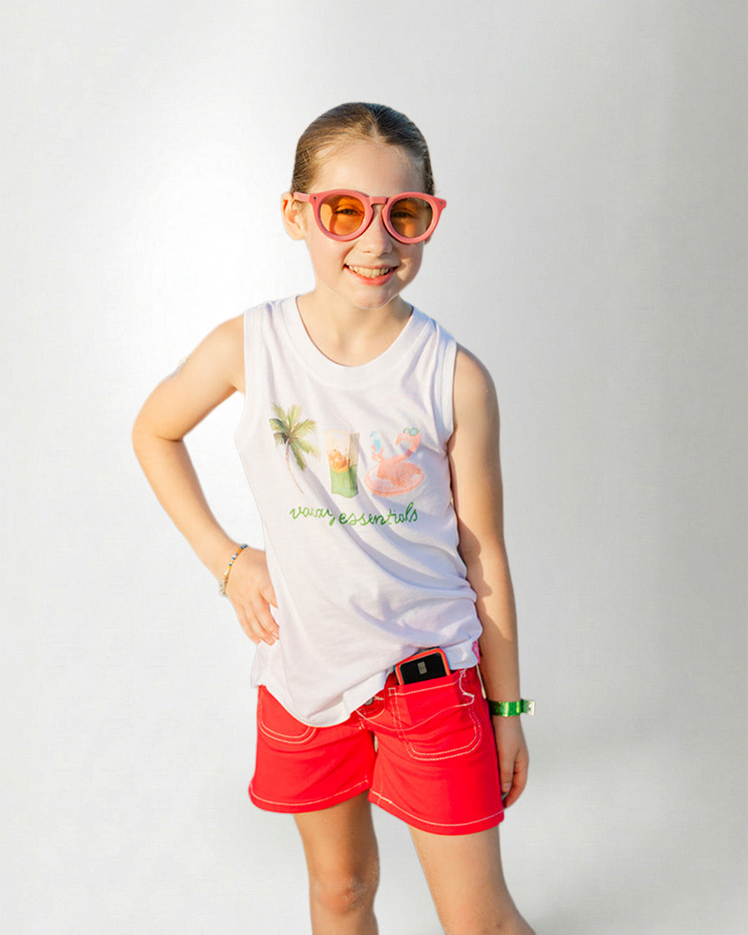 Young girl wearing a white sleeveless shirt with graphics and text, standing against a plain background