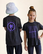 Two children wearing black t-shirts with purple text and a palm tree design on a plain background