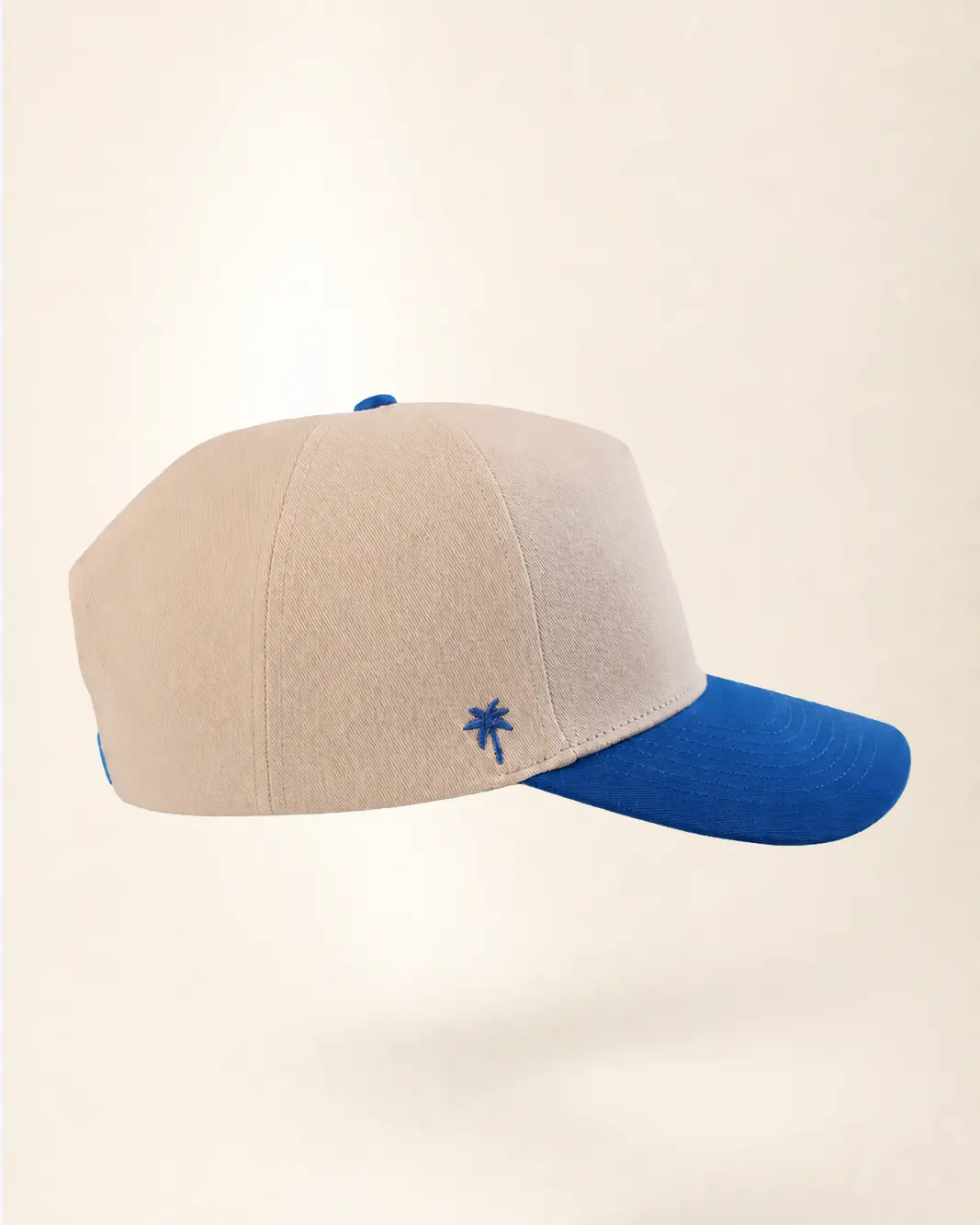 A beige baseball cap with a bright blue curved brim, blue button, and blue embroidered palm tree on the side, shown against a plain light beige background.