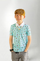 Young boy wearing a light blue polo shirt with colorful patterns on a plain background