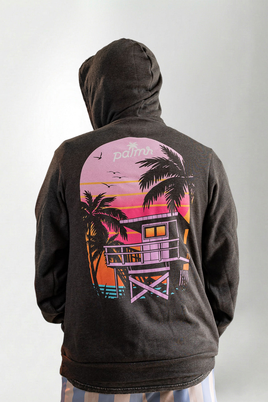 Black hoodie with a colorful beach scene design on the back, worn by a person.
