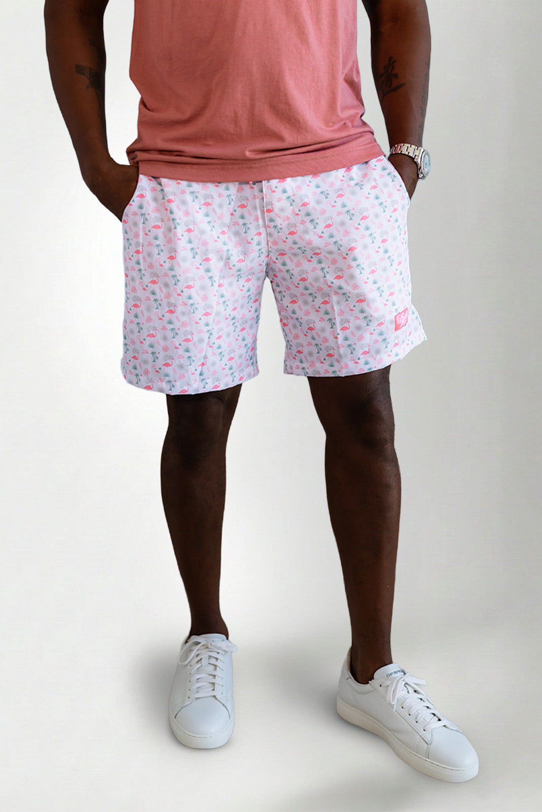 Person wearing pink floral shorts and white sneakers on a plain background
