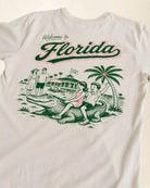 Welcome to Florida, Cream shirt showing a vintage style illustration of 2 kids riding a crocodile both smilind 