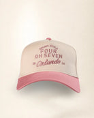 A two-tone baseball cap with a cream-colored crown and a pink brim, featuring pink embroidered text on the front that reads 'PALMIRE STYLE FOUR OH SEVEN 20 Orlando 24'.