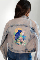 Denim jacket with a colorful parrot design on the back, worn by a person.