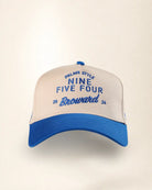 A two-tone baseball cap with a cream-colored front panel and a blue brim, featuring blue embroidered text that reads 'PALMR STYLE NINE FIVE FOUR Broward 2024'.