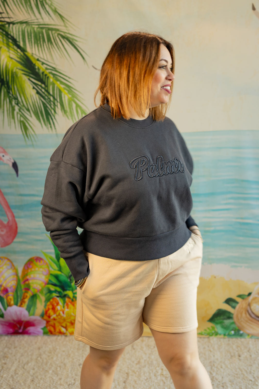 Person wearing a dark gray sweatshirt with 'Pullover' text, standing in front of a tropical-themed wall.