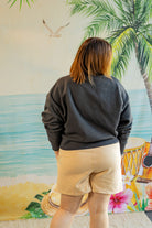 Person wearing a dark gray sweatshirt and beige shorts standing in front of a colorful mural with a beach scene.