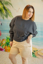 Woman wearing a dark gray sweatshirt with 'Palmer' text and beige shorts, standing in front of a colorful mural.