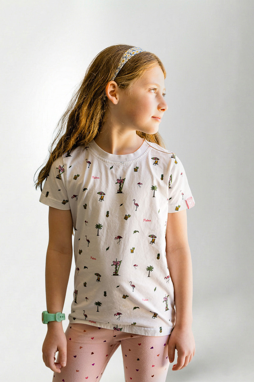Young girl wearing a patterned shirt and pink pants on a plain background