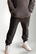 Person wearing a dark gray hoodie and pants with white sneakers on a light gray background